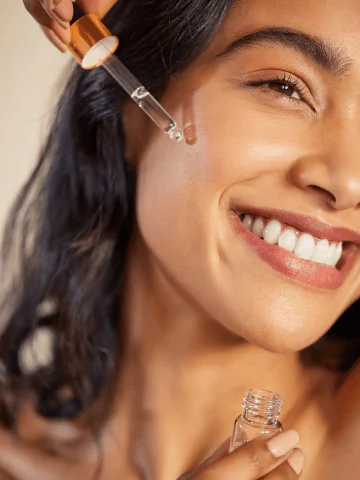 Smiling woman applying a face serum with a dropper