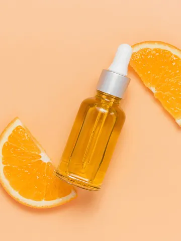Golden face serum in a glass dropper bottle with fresh orange slices